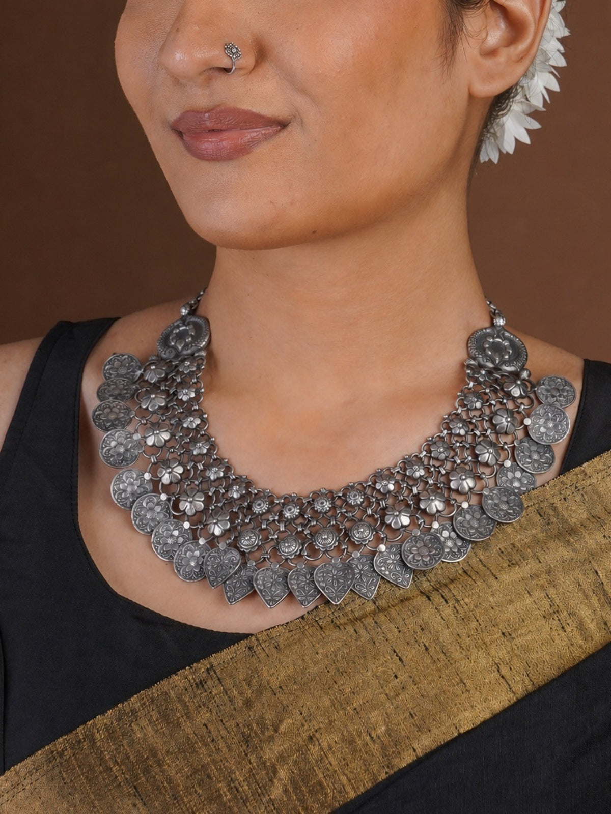 Close angled view of Sitavan oxidized collar necklace with floral mesh embossed coin motifs and engraved heart drops